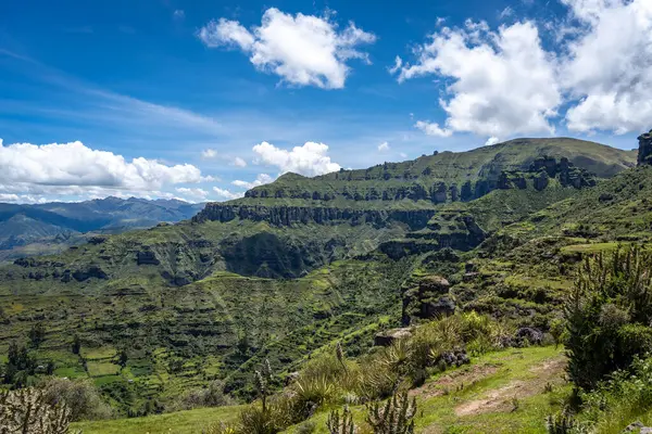 Peru 'daki Waqrapukara bölgesinde dramatik kaya oluşumları, yeşil vadiler ve dik uçurumlar yer almakta, And dağlarının parlak mavi gökyüzü altında nefes kesen manzaraları sunmaktadır.