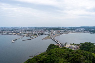 Adadan Enoshima şehrine bakan geniş bir kıyı manzarası kıvrımlı körfez, kentsel ufuk çizgisi, liman ve etrafındaki orman tepelerini ortaya çıkarıyor. Japonya