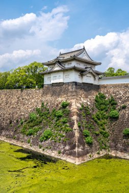 Savunma taş duvarları ve Osaka Kalesi 'nin geleneksel beyaz tareti, parçalı bulutlu bir gökyüzünün altındaki hendeğin sakin sularına yansıdı.