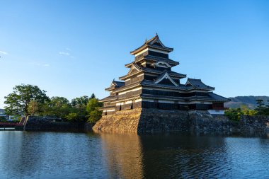 Matsumoto Şatosu, Japonya 'nın Matsumoto kentindeki karanlık ahşap dış yüzeyinden yansıyan altın ışıkla görkemli bir şekilde ayakta duruyor.