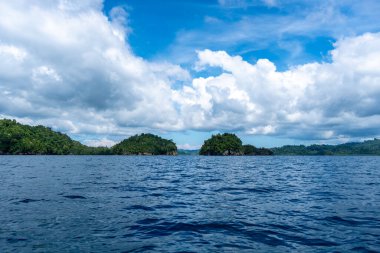 Togian Adaları, Sulawesi, Endonezya 'daki bulutlarla dolu gökyüzünün altındaki derin mavi sulardan küçük orman adaları yükselir.