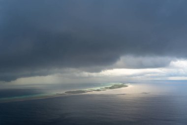 Tuamotus 'taki geniş Rangiroa adası kara fırtına bulutlarının altında belirir. Güneş ışığı turkuaz sulara yansıyarak ışık ve gölge arasında çarpıcı bir kontrastlık yaratır. Fransız Polinezyası.