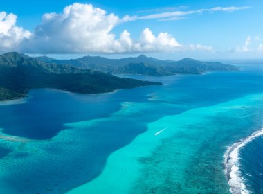 Fransız Polinezyası 'ndaki Tahaa adası, yukarıdan bakıldığında turkuaz bir göl, mercan resifi ve yemyeşil dağları ortaya çıkarır. Canlı okyanus renkleri koyu mavi Pasifik ile tezat oluşturuyor.