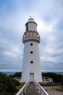 Avustralya 'daki Büyük Okyanus Yolu boyunca uzanan tarihi bir deniz feneri olan Otway Burnu bulutlu bir gökyüzüne karşı duruyor ve okyanus manzarası ve deniz tarihi sunuyor.
