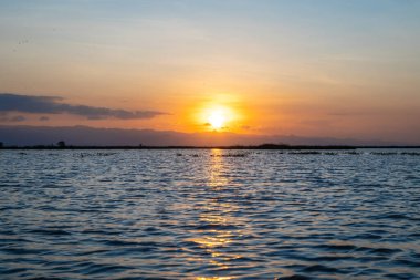 Tempe Gölü 'nün sakin suları, Endonezya' daki Sulawesi ufkunu canlı renkler ve yumuşak dalgalarla aydınlatan parlak günbatımını yansıtır.