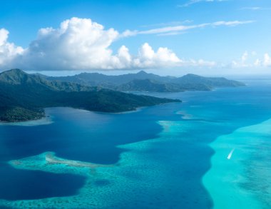 Fransız Polinezyası 'ndaki Tahaa adası, yukarıdan bakıldığında turkuaz bir göl, mercan resifi ve yemyeşil dağları ortaya çıkarır. Canlı okyanus renkleri koyu mavi Pasifik ile tezat oluşturuyor.