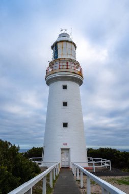 Avustralya 'daki Büyük Okyanus Yolu boyunca uzanan tarihi bir deniz feneri olan Otway Burnu bulutlu bir gökyüzüne karşı duruyor ve okyanus manzarası ve deniz tarihi sunuyor.