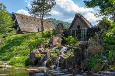 Küçük çağlayan bir şelale, Japonya 'nın Shirakawa-go kentindeki geleneksel go tarzı evler ve yemyeşil evlerle çevrili huzurlu bir gölete akar.