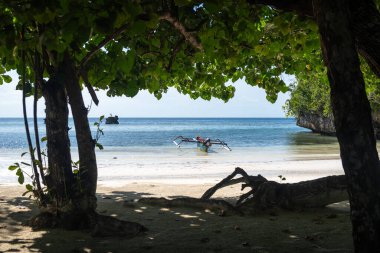 Geleneksel ahşap bir tekne, Lia sahilinin beyaz kumları yakınında, Waleakodi Adası, Togian takımadaları, Sulawesi, Endonezya 'da parlak mavi bir gökyüzünün altında yüzmektedir.
