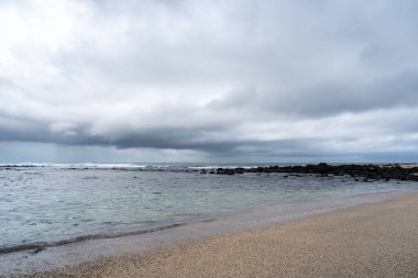 Galapagos, Ekvador 'daki San Cristobal Adası' ndaki Playa Loberia 'nın huzurlu plajı berrak suları ve dramatik gökyüzü ile huzurlu bir manzara sunuyor.