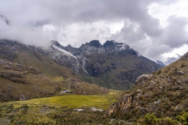 Engebeli arazisi, altın çayırları ve kısmen dramatik bulutlarla kaplı karlı tepeleri olan çarpıcı bir And Vadisi. Bu nefes kesici sahne, Huaraz, Peru 'daki Laguna 69 yürüyüşünün bir parçası.