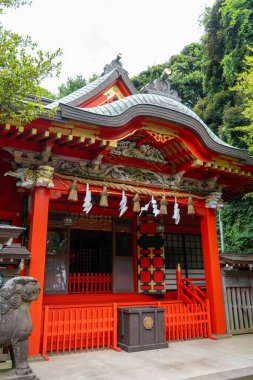 Enoshima-Shrine Nakatsunomiya 'nın parlak kırmızı ana salonu Japonya' nın Enoshima Adası 'ndaki ağaçlar, geleneksel fenerler ve koruyucu heykellerle çevrilidir.