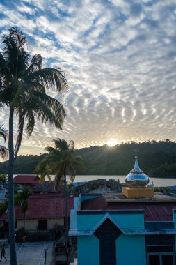 Pulau Papan camisi Endonezya 'nın Sulawesi kentindeki Malenge Adası üzerindeki sıcak günbatımı ışığında aydınlanan balıkçı evleri arasında yer alıyor.