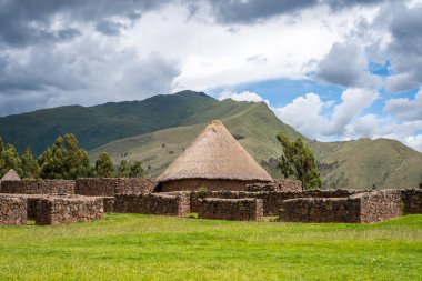 Peru 'daki Raqchi' nin tarihi mekanında antik İnka taş duvarları ve yeşil manzaralar ve And Dağları ile çevrili yeniden inşa edilmiş sazdan çatı kulübesi yer alıyor.