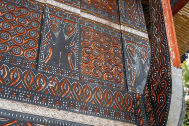 Geometrik desenler ve sembolik motifler geleneksel bir Toraja evinin ahşap panellerini süsler, Sulawesi halkının kültür ve inançlarını yansıtır.