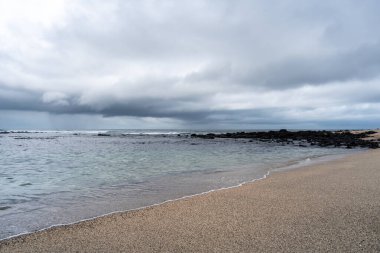 Galapagos, Ekvador 'daki San Cristobal Adası' ndaki Playa Loberia 'nın huzurlu plajı berrak suları ve dramatik gökyüzü ile huzurlu bir manzara sunuyor.