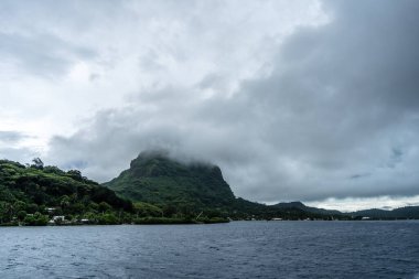 Bereketli dağları, berrak suları ve uzaktaki dramatik bulutlarıyla Bora Bora Adası 'nın çarpıcı panoramik manzarası.