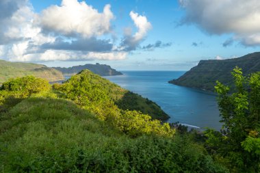 Altın ışık, Fransız Polinezyası 'nın Nuku Hiva kentindeki Taipivai Körfezi' nin yemyeşil tepelerini aydınlatırken okyanus dramatik bir gökyüzünün altında ufka doğru uzanıyor.