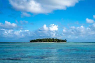 Tikehau mercan adasında çarpıcı bir slogan, Fransız Polinezyası, bereketli palmiye ağaçları, beyaz kum ve kristal berrak suları dağınık mavi bulutlar altında