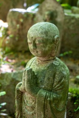 Japonya 'nın Hiroşima kentindeki Mitaki-Dera tapınak bahçesinin sessiz yeşilliklerine yerleşmiş dua eden bir keşişin huzur dolu yosun kaplı heykeli.