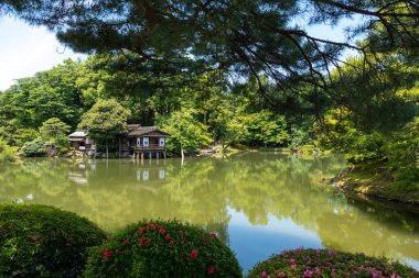 Kanazawa 'daki Kenroku-en Bahçesi tarihi Kanazawa Kalesi' nin yanında huzurlu bir su, yeşillik ve geleneksel yapılar manzarası sunuyor.