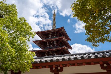 Shitenno-ji Tapınağı 'nın beş katlı tapınağı yeşil ağaçlar ve Osaka' daki bulutlarla dolu gökyüzü tarafından çerçevelenmiş tapınak duvarlarının üzerinde yükseliyor.