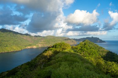 Altın ışık, Fransız Polinezyası 'nın Nuku Hiva kentindeki Taipivai Körfezi' nin yemyeşil tepelerini aydınlatırken okyanus dramatik bir gökyüzünün altında ufka doğru uzanıyor.
