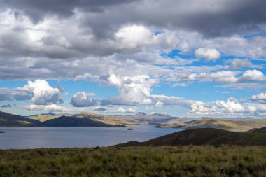 Peru 'daki Lagunillas Gölü, üzerinde kara fırtına bulutları ve dağların üzerine yağan yağmur yağmuru ile yuvarlanan tepeler ve otlaklarla çevrilidir.