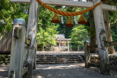 Shirakawa-go köyündeki Shirakawa Hachiman Tapınağı 'nın girişini gösteren kutsal ip ve kağıt kalkanla süslenmiş taş torii kapısı.