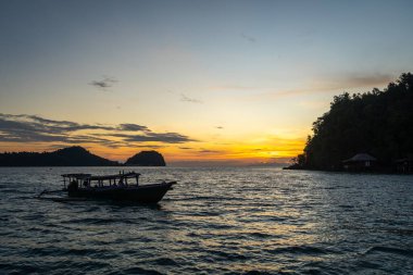 Gün batımında Bolilanga Adası, Togian takımadaları, Sulawesi, Endonezya sahillerinde sakin suları ve altın gökyüzü ile küçük bir tekne huzur içinde yüzer.