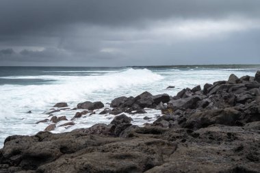 San Cristobal, Galapagos 'taki huzurlu Playa Loberia plajı, kayalık kıyı şeridi ve okyanus üzerindeki kara bulutlarıyla, sakin bir atmosfer yaratıyor.
