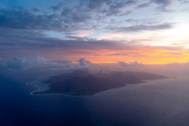 Gün batımında yukarıdan görülen Moorea adası engebeli tepelerini, etrafını çevreleyen lagünü ve sıcak altın ve mavi renklerle yıkanmış dramatik kıyı şeridini gözler önüne serer.