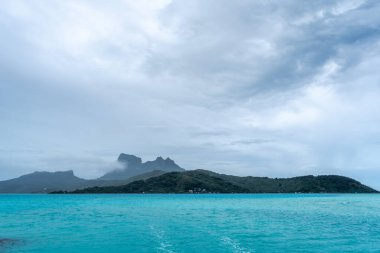 Bereketli dağları, berrak suları ve uzaktaki dramatik bulutlarıyla Bora Bora Adası 'nın çarpıcı panoramik manzarası.