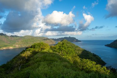 Altın ışık, Fransız Polinezyası 'nın Nuku Hiva kentindeki Taipivai Körfezi' nin yemyeşil tepelerini aydınlatırken okyanus dramatik bir gökyüzünün altında ufka doğru uzanıyor.