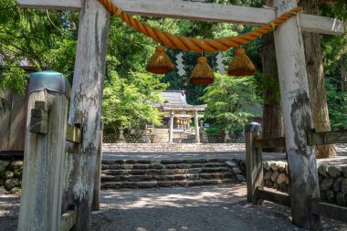 Shirakawa-go köyündeki Shirakawa Hachiman Tapınağı 'nın girişini gösteren kutsal ip ve kağıt kalkanla süslenmiş taş torii kapısı.
