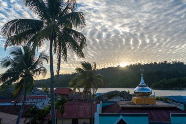 Pulau Papan camisi Endonezya 'nın Sulawesi kentindeki Malenge Adası üzerindeki sıcak günbatımı ışığında aydınlanan balıkçıların evleri arasında yer alıyor.