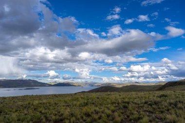 Peru 'daki Lagunillas Gölü, üzerinde kara fırtına bulutları ve dağların üzerine yağan yağmur yağmuru ile yuvarlanan tepeler ve otlaklarla çevrilidir.