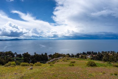Amantani Adası, Peru 'da küçük bir köy, tarımsal tarlaları ve dağınık evleri olan, Titicaca Gölü' nün sakin sularına bakan bulutlarla dolu bir gökyüzü.