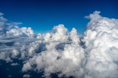 Yükselen beyaz bulutlar, bir uçaktan alınan derin mavi gökyüzüne doğru yükseliyor. Havadan bakıldığında gökyüzünün enginliği ve güzelliği vurgulanıyor.