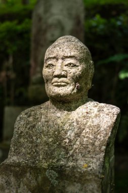 Hiroşima 'daki Mitaki-Dera Tapınağı' nda orman gölgesiyle çevrili yıpranmış bir heykel huzur içinde duruyor.