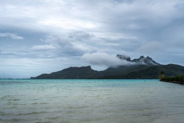 Bereketli dağları, berrak suları ve uzaktaki dramatik bulutlarıyla Bora Bora Adası 'nın çarpıcı panoramik manzarası.