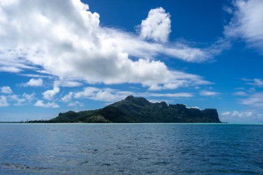Fransız Polinezyası 'ndaki Maupiti Adası' nın göz kamaştırıcı manzarası. Beyaz bir kumsal sahili, turkuaz lagün suları ve arka planda yemyeşil dağlarla kaplı.