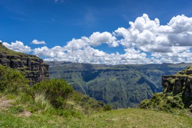 Waqrapukara arkeolojik alanını çevreleyen yeşil dağ tepeleri ve sarp kayalıklar, And 'ın berrak mavi gökyüzü altında nefes kesici panoramik manzaralar sunuyor.