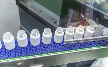 Otomatik sıvı dolum makinesinin taşıyıcı bandında polipropilen beyaz şişeler taşınıyor