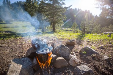 Yürüyüş sırasında kamp ateşinde yanan turistik çaydanlık. Ormanda odun üzerinde yemek pişirmek..
