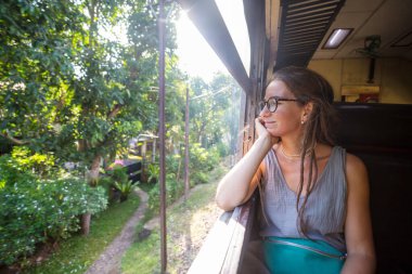 Sri Lanka 'nın dağlık bölgelerindeki çay tarlaları arasında Ella' dan Kandy 'ye tren yolculuğunun tadını çıkaran genç bir kadın.