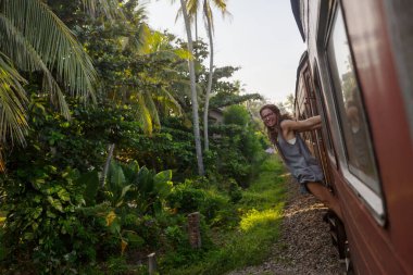 Sri Lanka 'nın dağlık bölgelerindeki çay tarlaları arasında Ella' dan Kandy 'ye tren yolculuğunun tadını çıkaran genç bir kadın.