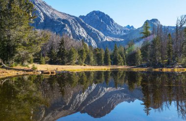 Sakin sulardaki kayaların yansımasıyla dağdaki gölün sakin manzarası..