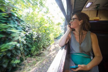 Sri Lanka 'nın dağlık bölgelerindeki çay tarlaları arasında Ella' dan Kandy 'ye tren yolculuğunun tadını çıkaran genç bir kadın.