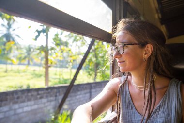 Sri Lanka 'nın dağlık bölgelerindeki çay tarlaları arasında Ella' dan Kandy 'ye tren yolculuğunun tadını çıkaran genç bir kadın.